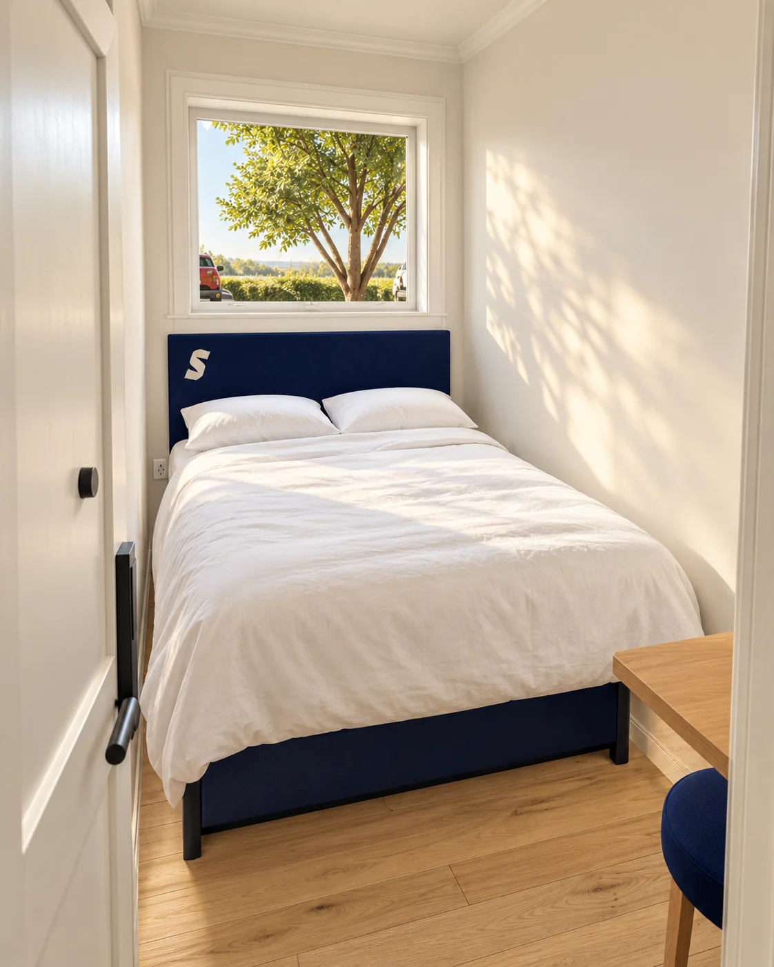 Architectural rendering of a compact room with a white duvet, navy headboard, oak floor and fold-away desk visible at the right